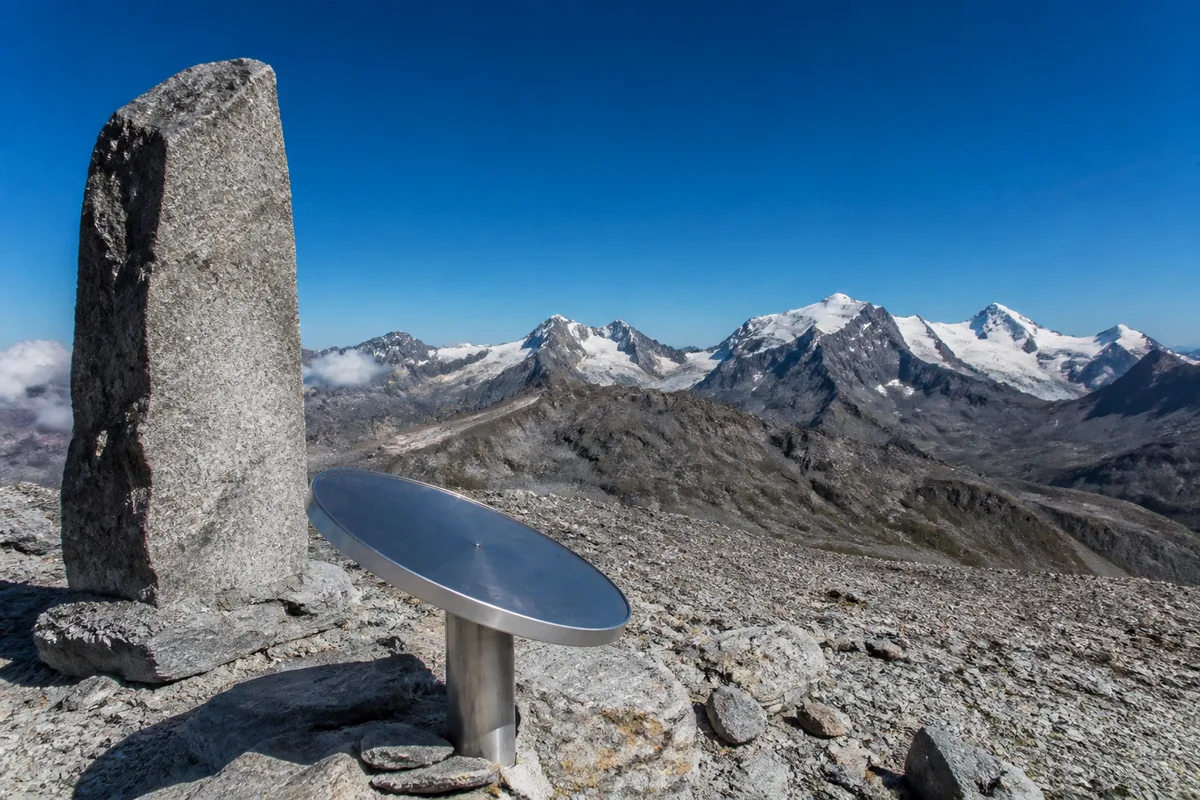 Stèle de pierre et table d’orientation au sommet d’un col alpin face aux glaciers